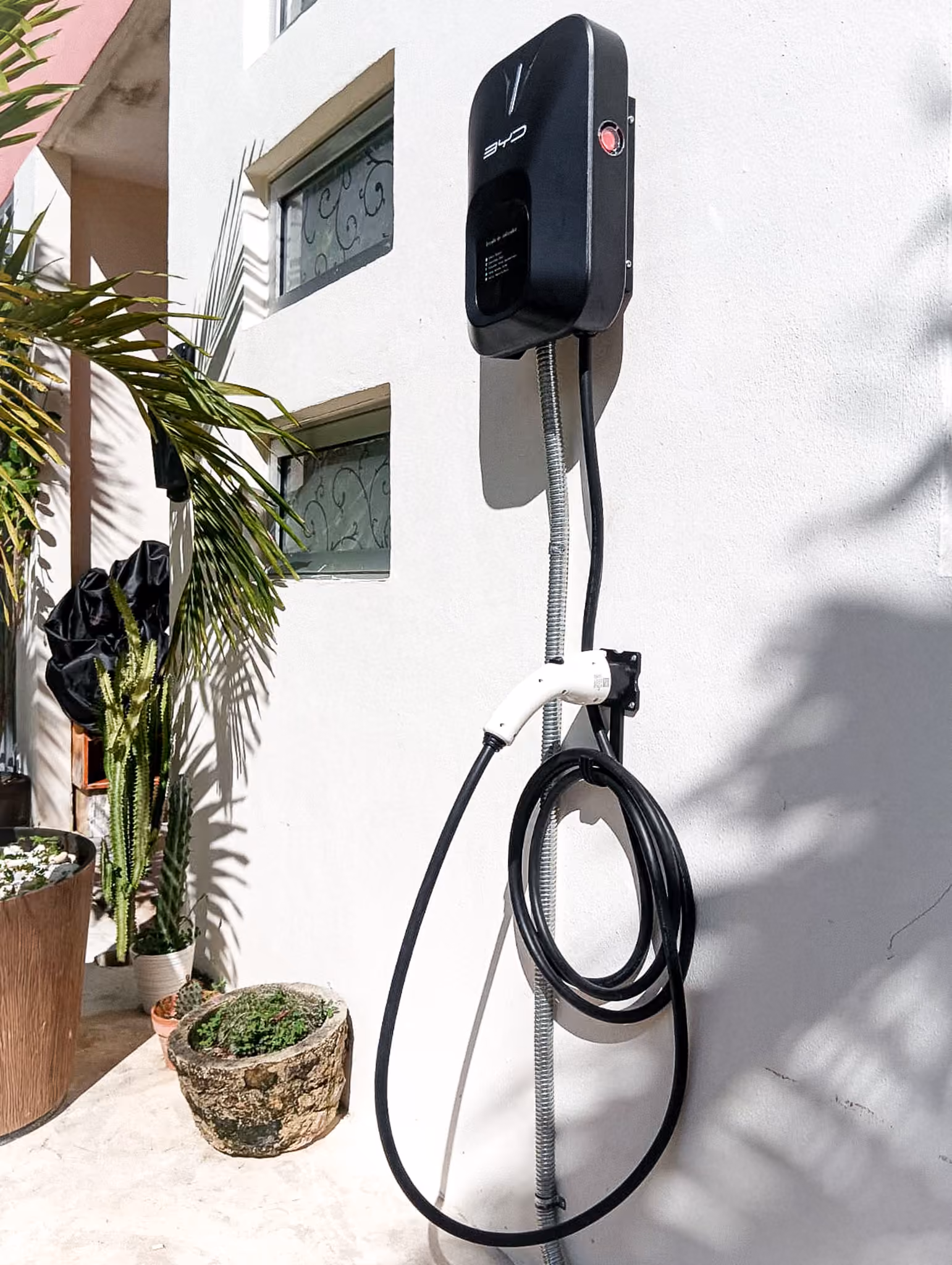 Cargador BYD montado en la fachada exterior de una casa, con canalización flexible a la vista.